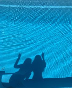 the shadow of two people standing in front of a swimming pool with their hands up