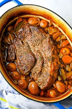 a pot filled with meat and vegetables on top of a blue table cloth next to a spoon