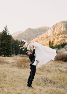 a bride and groom holding each other in an open field with mountains in the background