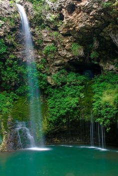 there is a large waterfall in the middle of the water with green trees around it