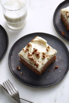 two black plates topped with slices of cake next to a glass of milk and fork