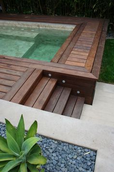 a wooden bench sitting next to a pool in a yard with gravel and rocks on the ground