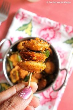 a person holding up some food on a stick in front of a bowl full of other food