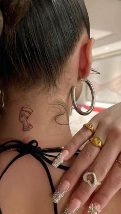 the back of a woman's head with tattoos on her neck and two rings around her neck