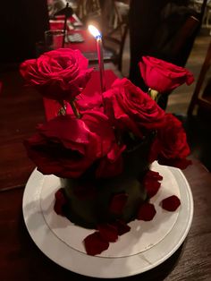 red roses in a black vase on a white plate with a lit candle and napkins