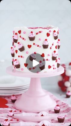 a white cake with pink frosting and cupcakes on it