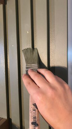 a person's hand holding a paintbrush in front of a metal wall with bars on it