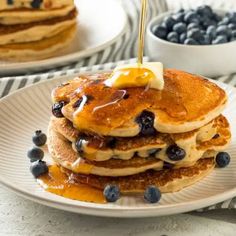 stack of pancakes with blueberries and syrup being drizzled on top