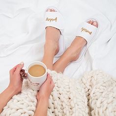 two people are laying in bed with their feet up on the blanket and holding a cup of coffee