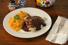 a white plate topped with meat covered in gravy next to rice and carrots