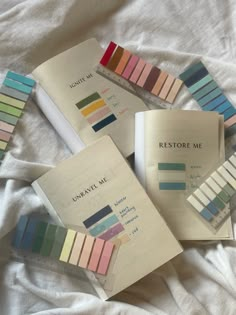 four books with different colors on them sitting on top of a white bed sheet, next to each other