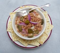 a white bowl filled with beans and onions next to crackers on top of a plate