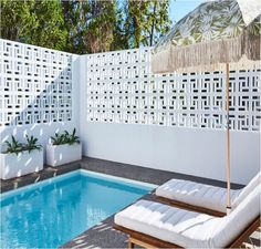 an outdoor swimming pool with lounge chairs, umbrella and planters on the side wall