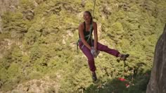 a woman on a rope high up in the air with her feet hanging down and smiling at the camera