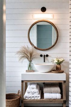 a white sink sitting under a round mirror next to a wooden shelf filled with towels