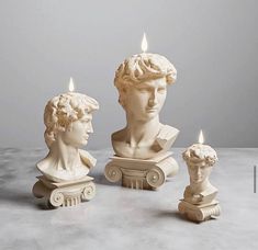 three white marble busturines sitting next to each other with candles burning in them