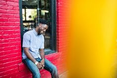 a man sitting on the side of a building next to a yellow and red wall