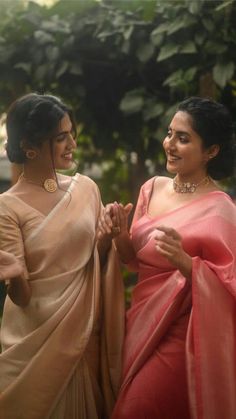 two women in sari standing next to each other and one is holding her hands together