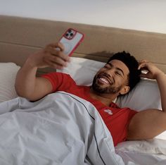 a man laying in bed while holding a cell phone up to his ear and smiling