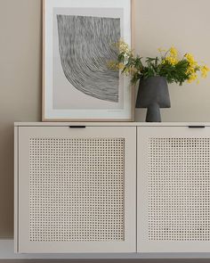 a vase with flowers sitting on top of a white cabinet next to a framed print