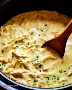 a wooden spoon is in a crock pot filled with chicken and cheese sauce, garnished with parsley