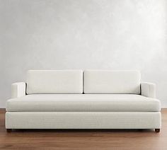 a white couch sitting on top of a hard wood floor next to a wall in an empty room