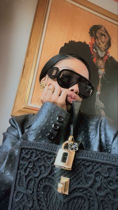 a woman in black leather jacket and sunglasses holding up her hand to her face with a lock on it