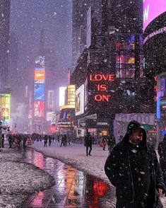 people walking in the snow on a city street at night with neon signs and buildings