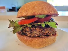 a burger with lettuce, tomato and meat on a bun sitting on a plate