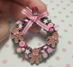 a hand holding a pink and white christmas wreath ornament with gingerbreads on it