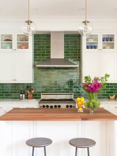 a kitchen with two stools in front of a counter and green tile backsplash