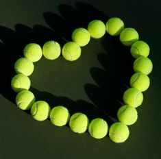 several tennis balls arranged in the shape of a heart on a green surface with shadow