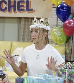 a woman wearing a crown standing in front of a table filled with presents and balloons