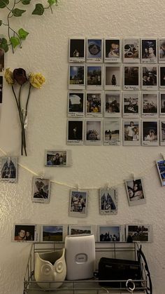 a bunch of pictures hanging on the wall above a shelf with flowers and other items