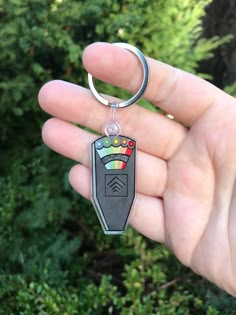 a hand holding a keychain with an object in it's center and trees in the background