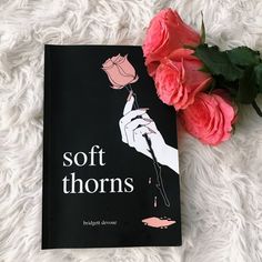 a pink rose sitting next to a soft thorns book