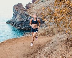 a woman running down a dirt road next to the ocean