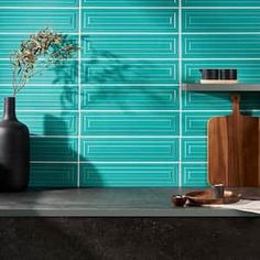 a black vase sitting on top of a table next to a blue wall with green tiles