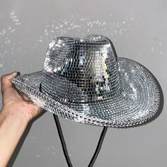 a person's hand holding up a shiny silver hat that is falling into the air