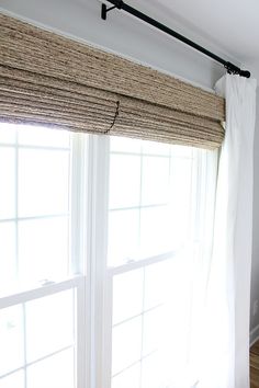 a bedroom with white walls and wooden flooring next to a window covered in roman shades