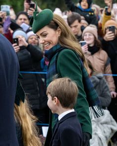 a woman in a green coat and hat standing next to a young boy