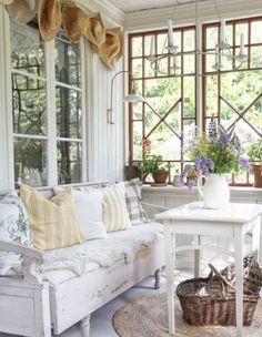 a living room filled with white furniture and lots of flowers on the window sill