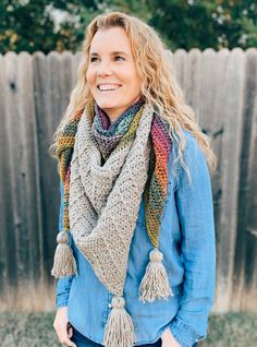 a woman standing in front of a fence wearing a scarf with tassels on it