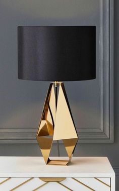 a gold table lamp with a black shade on the top and white drawers below it