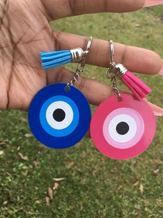 two handmade evil eye keychains with tassels in the palm of a person's hand