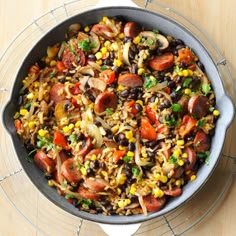 a skillet filled with rice, beans, and veggies on top of a wooden table