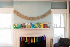 there is a birthday banner on the mantle in this living room with books and toys