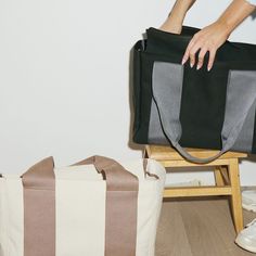 a person holding onto a black and white bag on top of a wooden chair next to a canvas bag