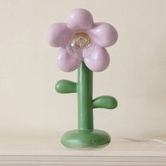 a green table lamp with a pink flower on it's base and a white wall in the background