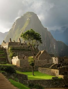 an old stone building with a tree in the foreground and mountains in the background